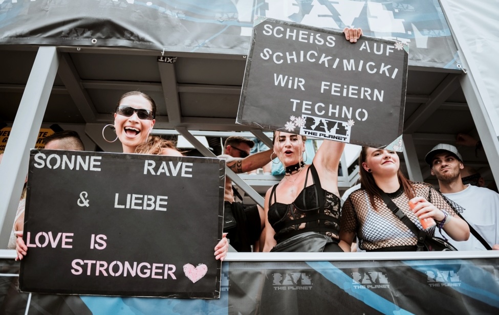 Junge Leute feiern bei Rave the Planet und halten Demoschilder hoch
