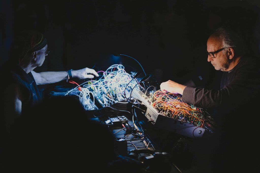 Das Duo Sunroof vor mehreren Synthesizern.